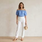 Woman in blue off-shoulder summer top with white tailored trousers and tan mules